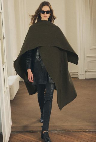 One of the best jacket coat brands, Zara, is shown in an image of a model wearing a green cape coat over a leather blazer, leather pants, and black heels