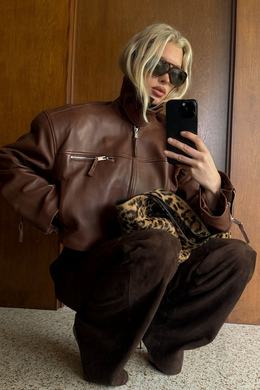 a woman wearing a brown leather jacket, brown pants, and cheetah print bag