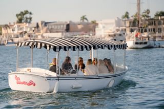 A Duffy boat with a black and white striped awning on the water in Newport Beach, California
