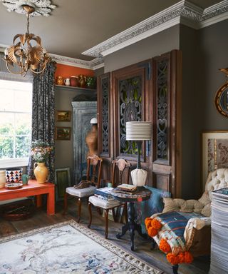 A living room in a whimsical Gothic style with intricate wooden furniture, layered textiles and a rich color palette