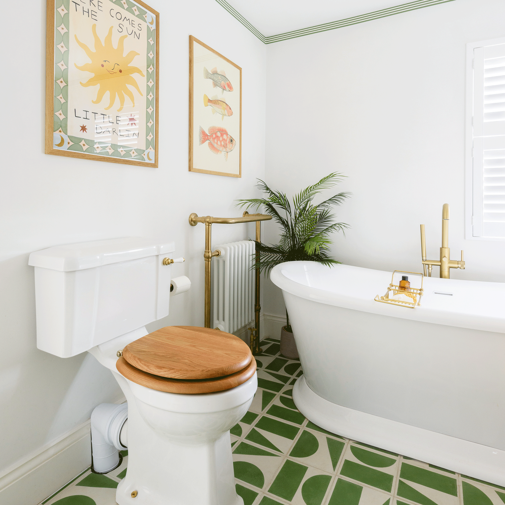 a white bathroom with green and cream tiled patterned flooring with a loo, freestanding bath and radiator with towel rail