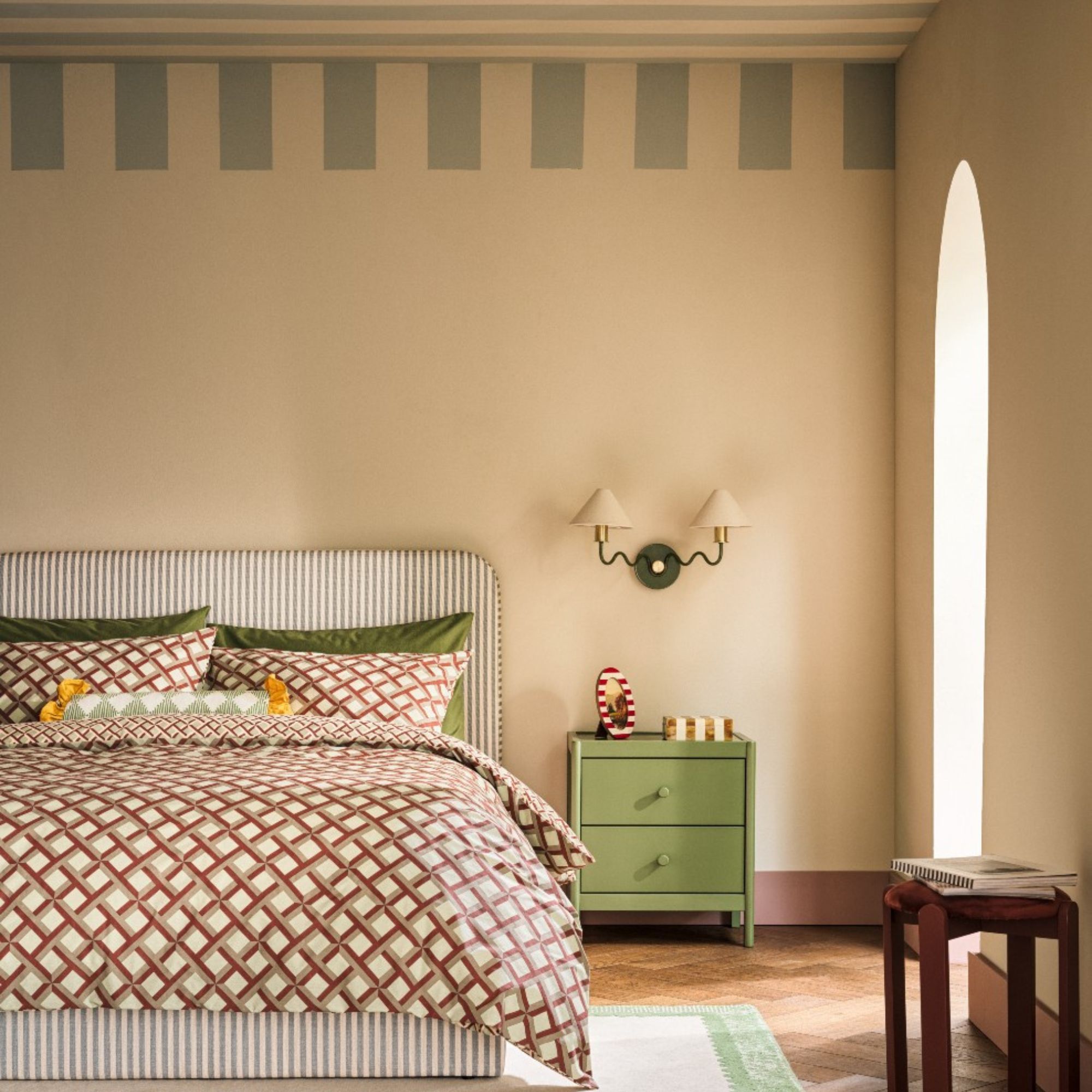 Habitat Wiggle Metal 2 Light Wall Light - Green & Natural hanging on beige wall above green bedside table, beside green striped headboard with red patterned sheets