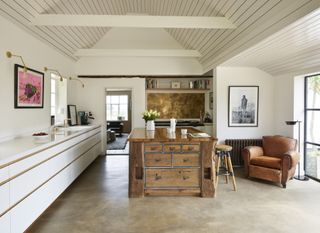 A rustic island unit made from salvaged oak beams, fused with hand-welded metalwork in a large kitchen with white cabinets