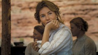 Sienna Miller sits posing her face on her hand, smiling wistfully in Horizon: An American Saga - Chapter 1.