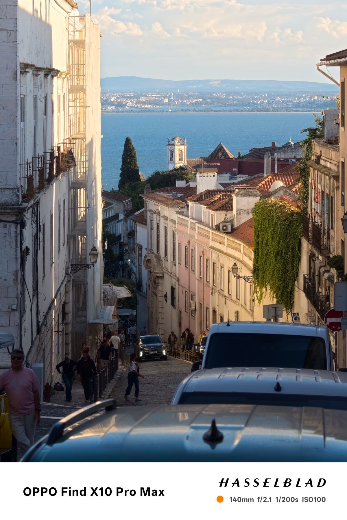Steep Lisbon street descending toward the river, framed by historic buildings in warm evening light.