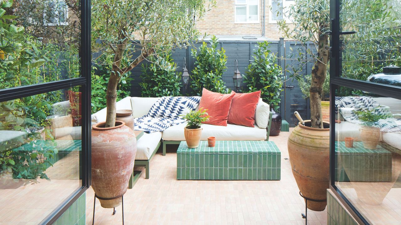 Small tiled patio garden with garden furniture and large pots with a fence at the back