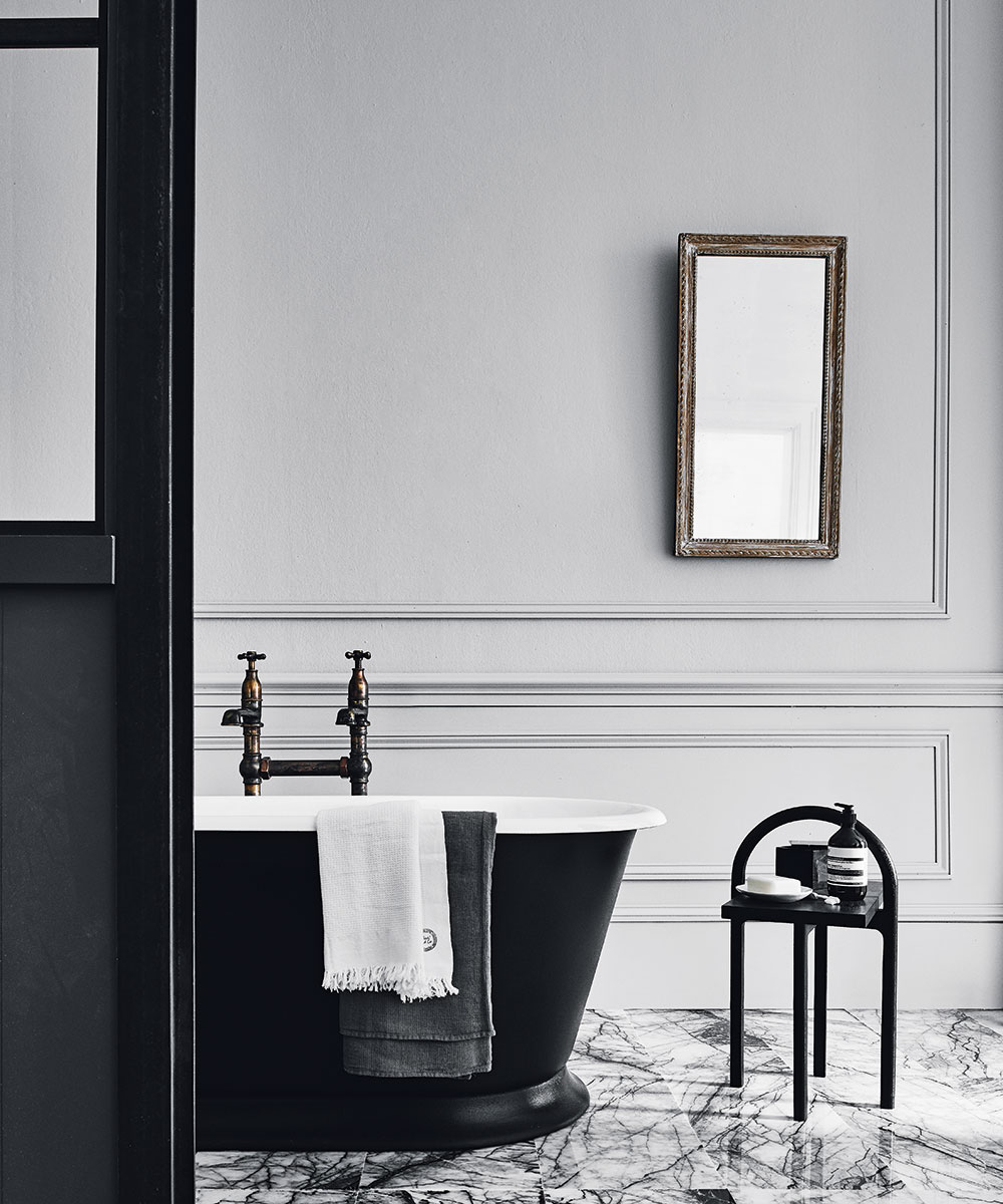 A black roll top bath in a bathroom with marble flooring and light grey walls