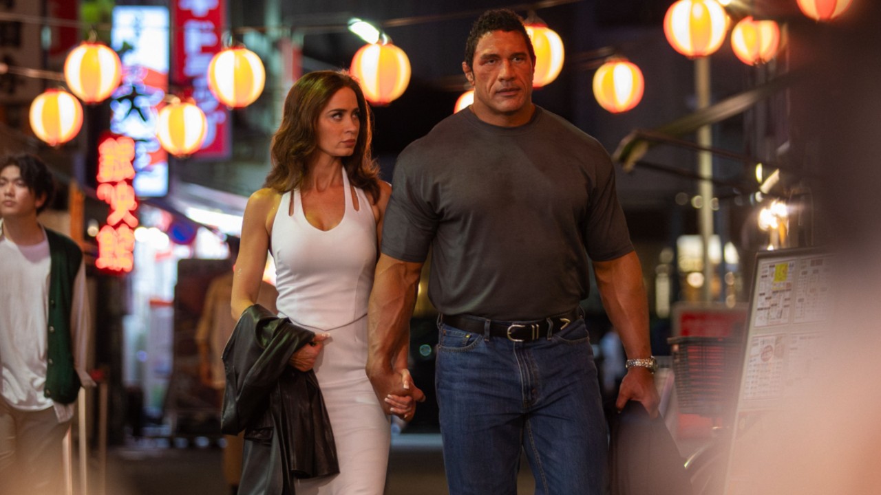 From left to right: Emily Blunt walking and holding hands with Dwayne Johnson in The Smashing Machine. 