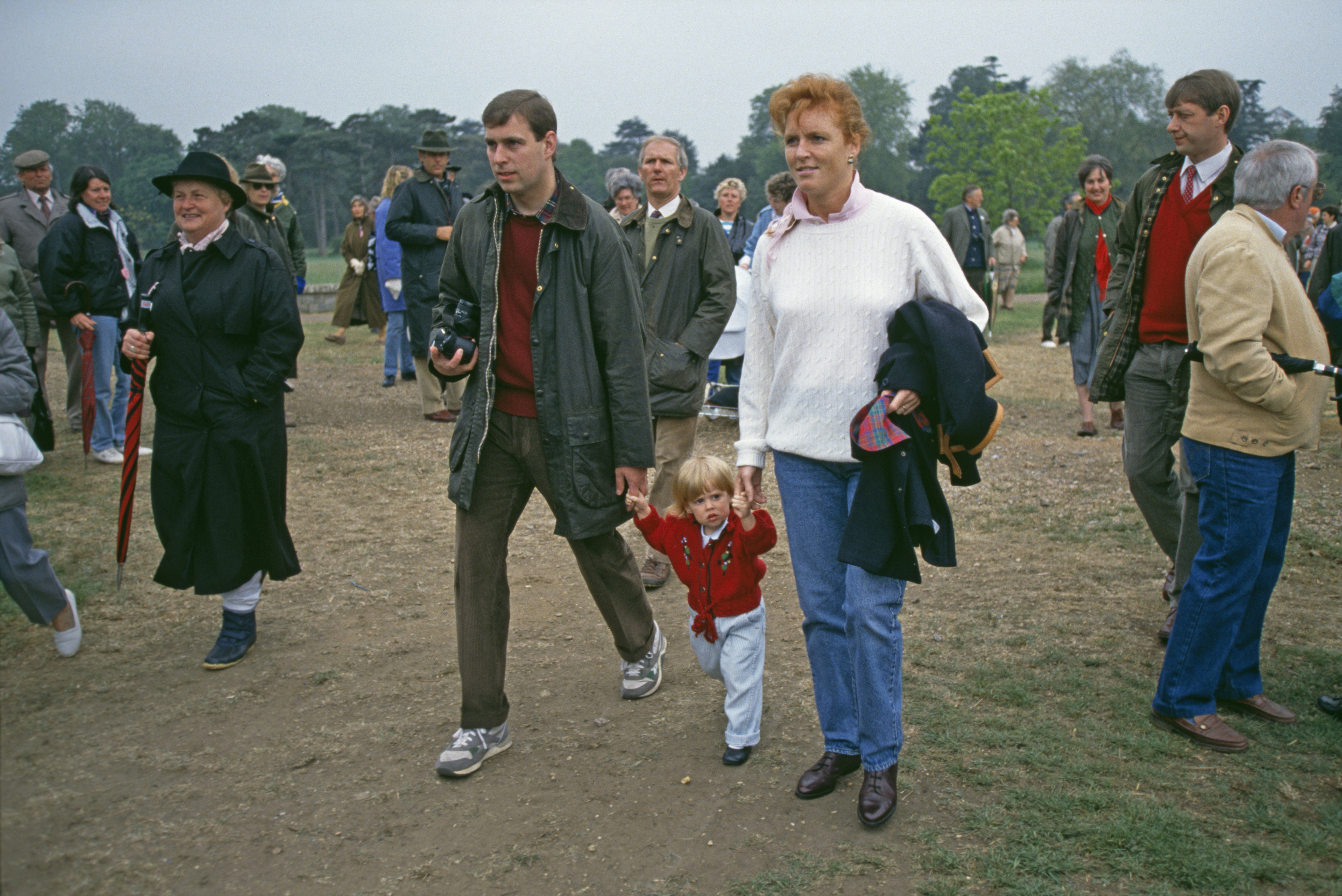 Sarah Ferguson and Prince Andrew holding hands with Princess Beatrice, walking in between them across grass, at the Royal Windsor Horse Show in 1990
