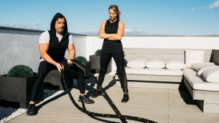 Man uses battle ropes on outdoor terrace while woman looks on