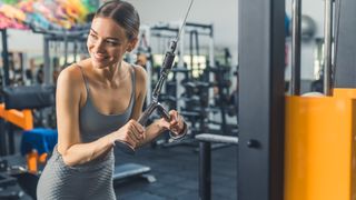 Woman smiling looking over her shoulder holding onto a cable machine attachment during workout