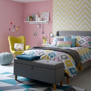 bedroom with pink and yellow designed wall grey bed with colourful cushion and wooden flooring