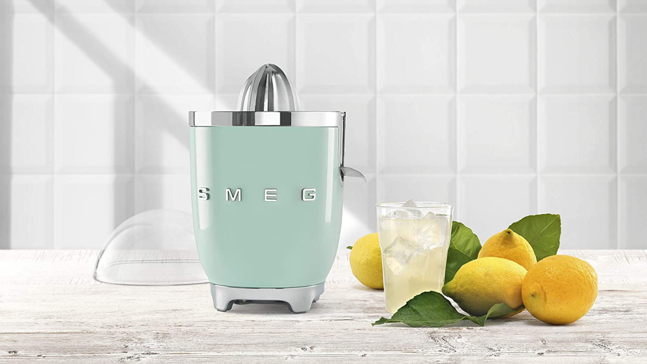 Smeg Citrus Juicer in pastel green, next to a trio of fresh lemons and a glass of lemonade 