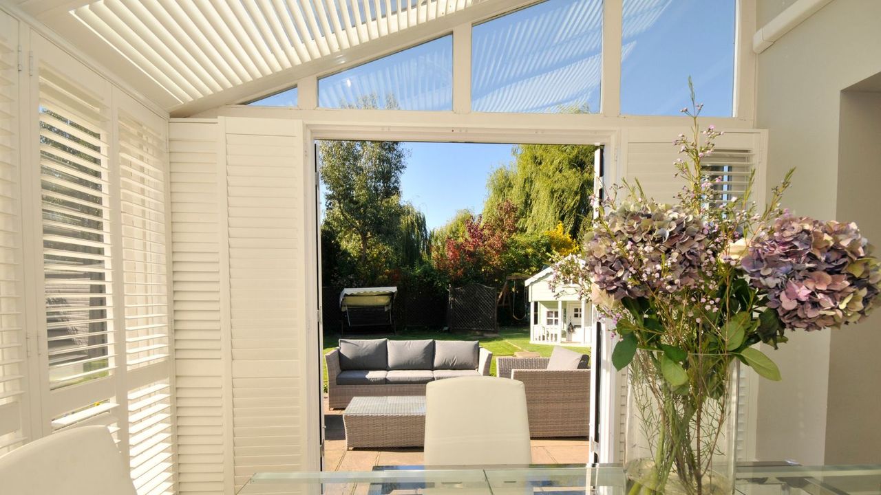 A sunroom, shielded by blinds, with open doors and a garden view.