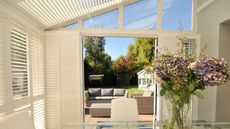 A sunroom, shielded by blinds, with open doors and a garden view.