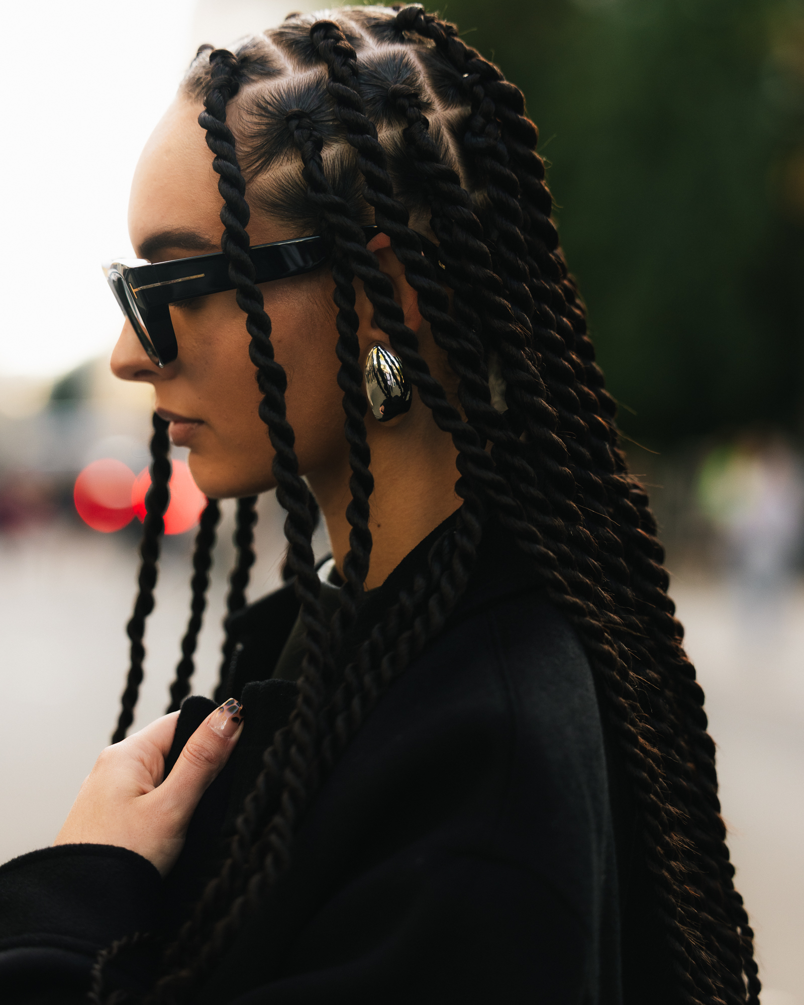 a woman with long twists, large sunglasses, and a black jacket