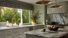 A light green kitchen with textured concrete on the island and range hood, paired with marble countertops