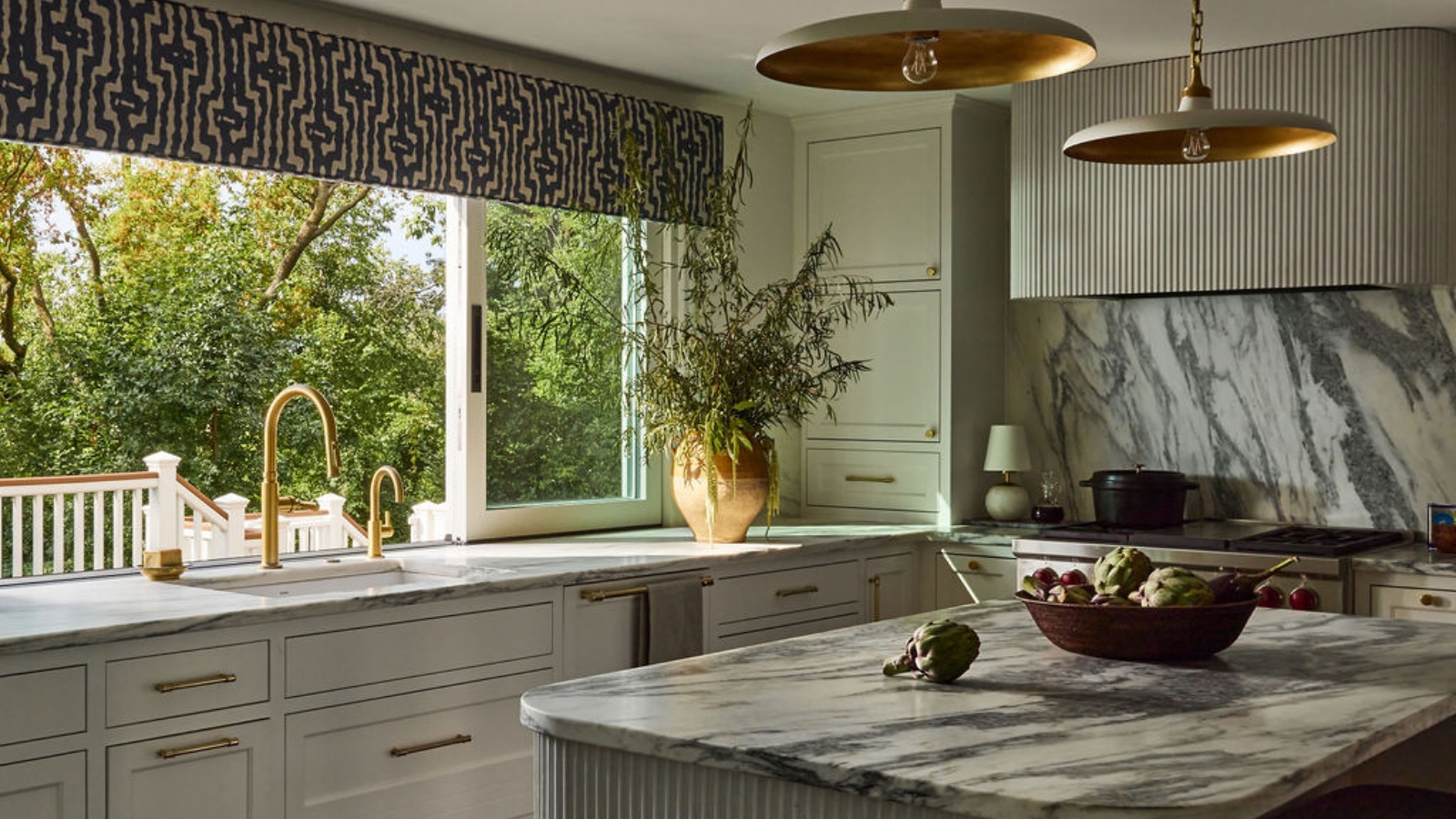 A light green kitchen with textured concrete on the island and range hood, paired with marble countertops