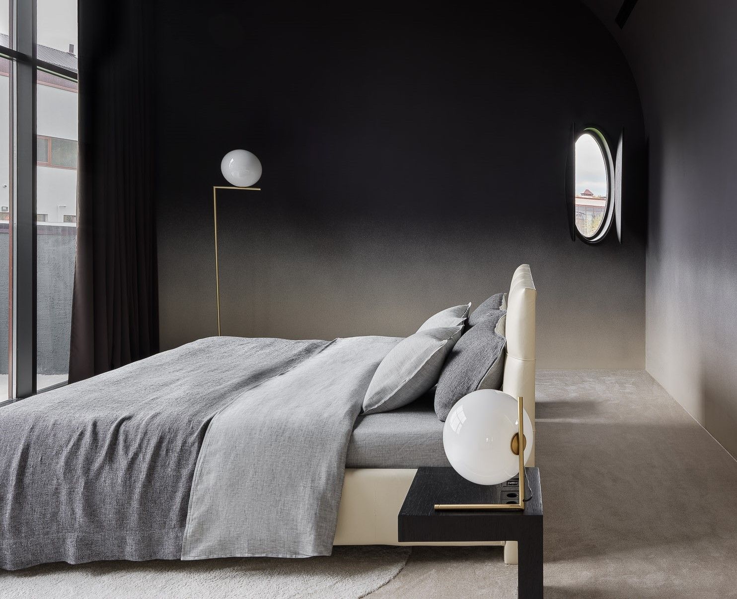 A dark, black toned bedroom with a freestanding bed placed in the centre