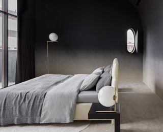 A dark, black toned bedroom with a freestanding bed placed in the centre