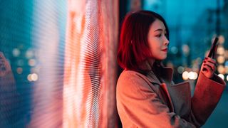 A woman holding her phone while leaning against a digital wall