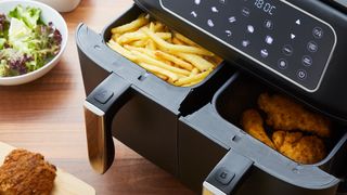 Swan air fryer with food inside the tray and food on the counter next to it