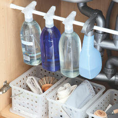 loseup of interior of kitchen sink cupboard, plastic baskets containing cleaning products, plastic rod running across cupboard to hang bottles