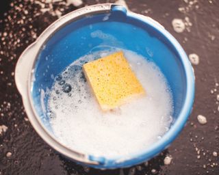 A blue bucket of soapy water with yellow sponge floating in white bubbles