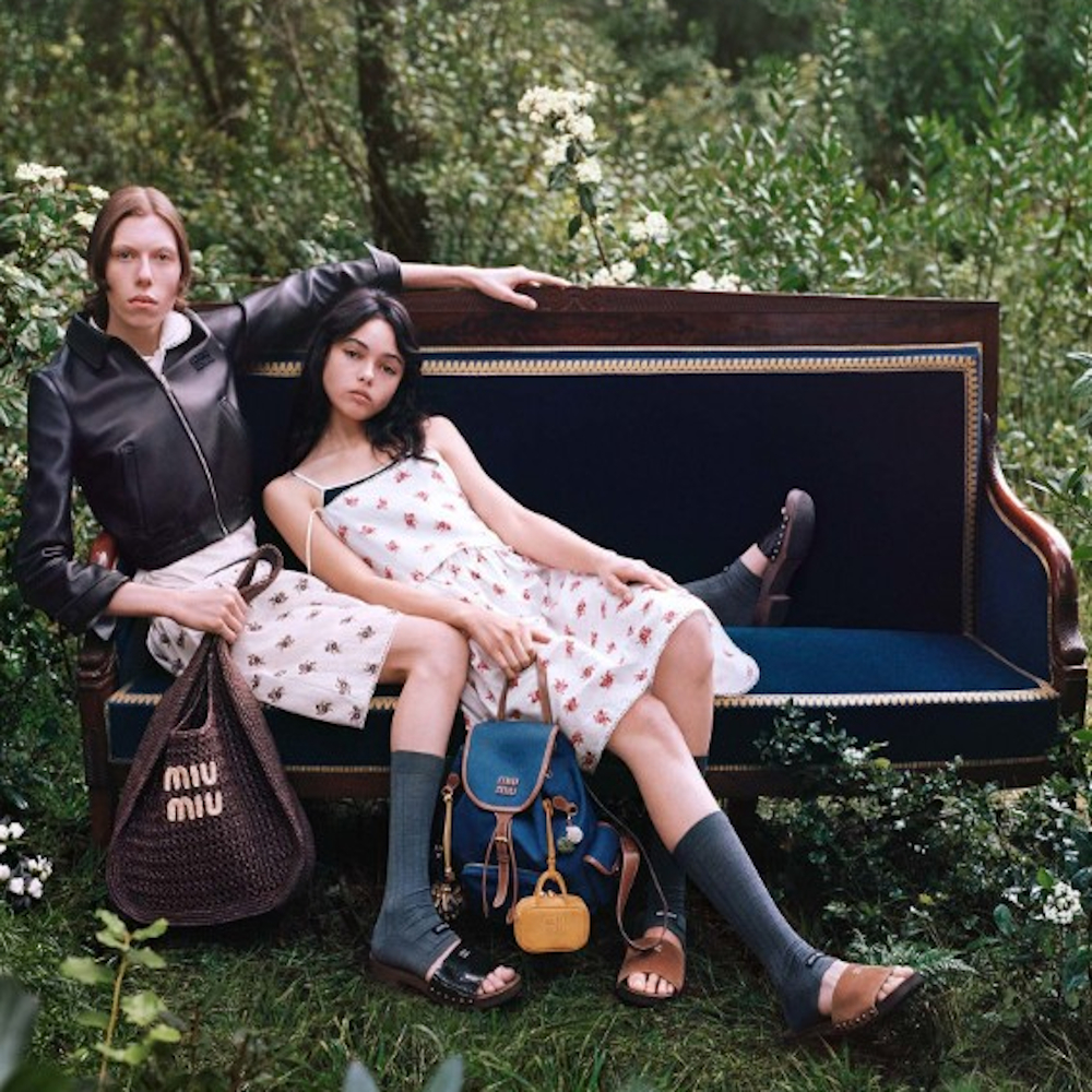Two women modelling Bergdorf Goodman dresses sat on a bench in a garden