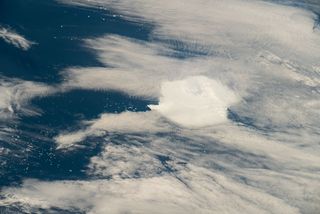 a white clump of iceberg sits below wispy clouds