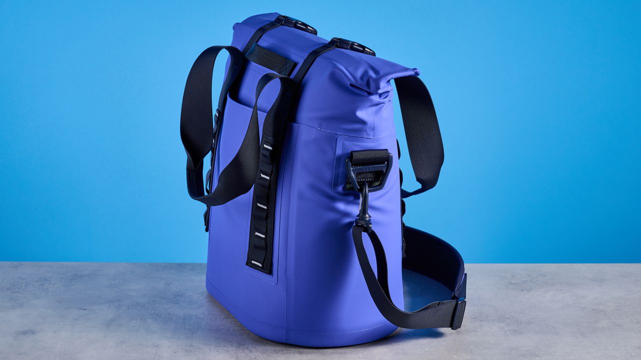 the yeti hopper m15 cool bag with a padded carry strap, handles, and a 15 quart capacity photographed with coke zero cans against a blue background