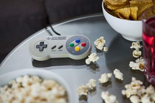 A vintage Nintendo SNES controller photographed on a glass table, surrounded by bowls of snacks