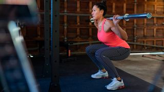 Woman performing the back squat with an empty barbell