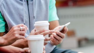 Couple drink takeaway coffees whilst looking on their phones