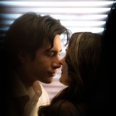 Hudson Williams and Carrie Ann Moss stand closely together in front of window blinds, seen through shadows, in the Crave tv show 'Yaga.'