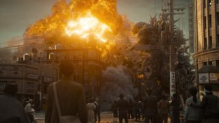 Pedestrians watching on as Godzilla wrecks buildings.