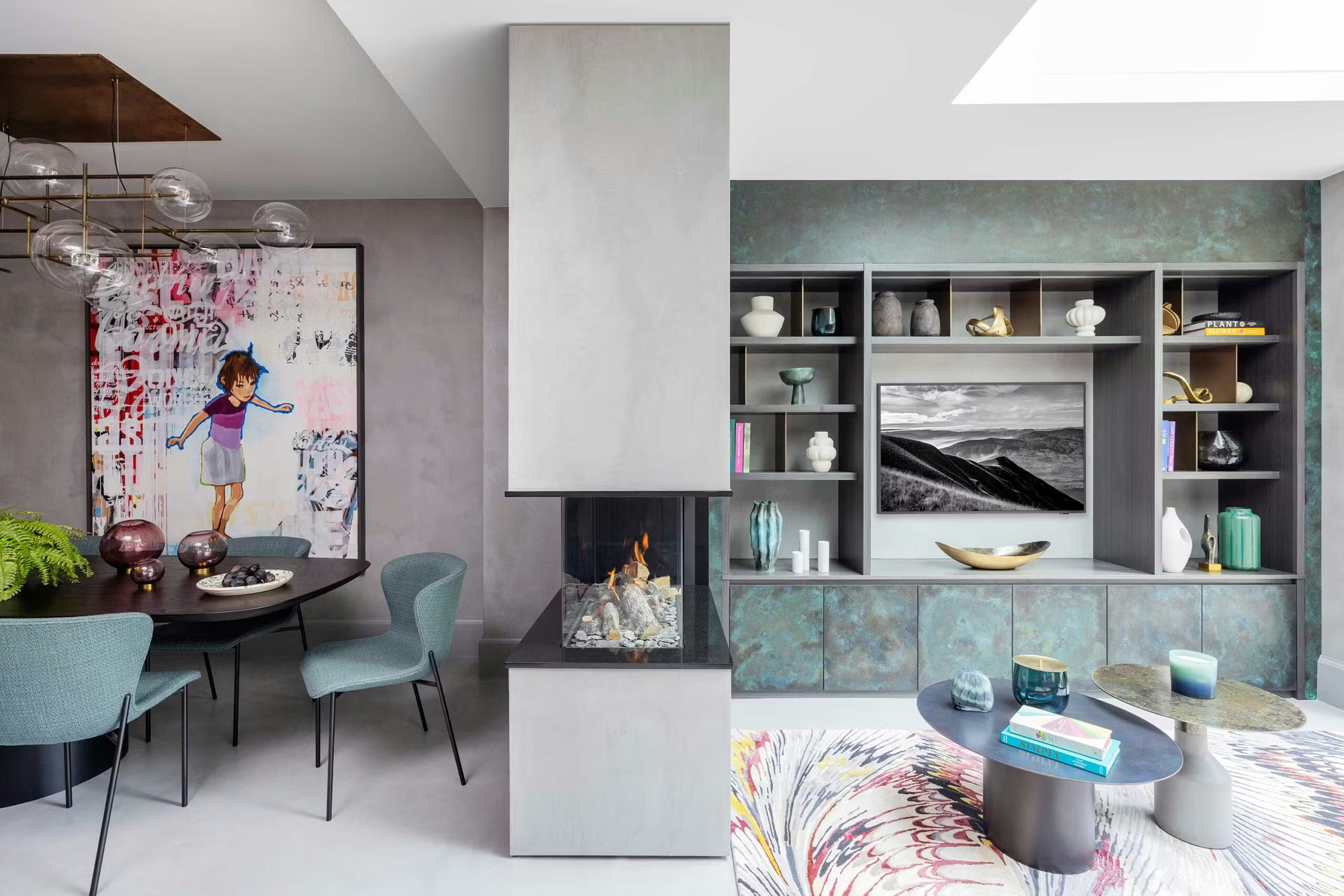 double-sided fireplace with built-in bookcase around TV on one side, and dining table with teal dining chairs around a black dining table with large artwork on the other