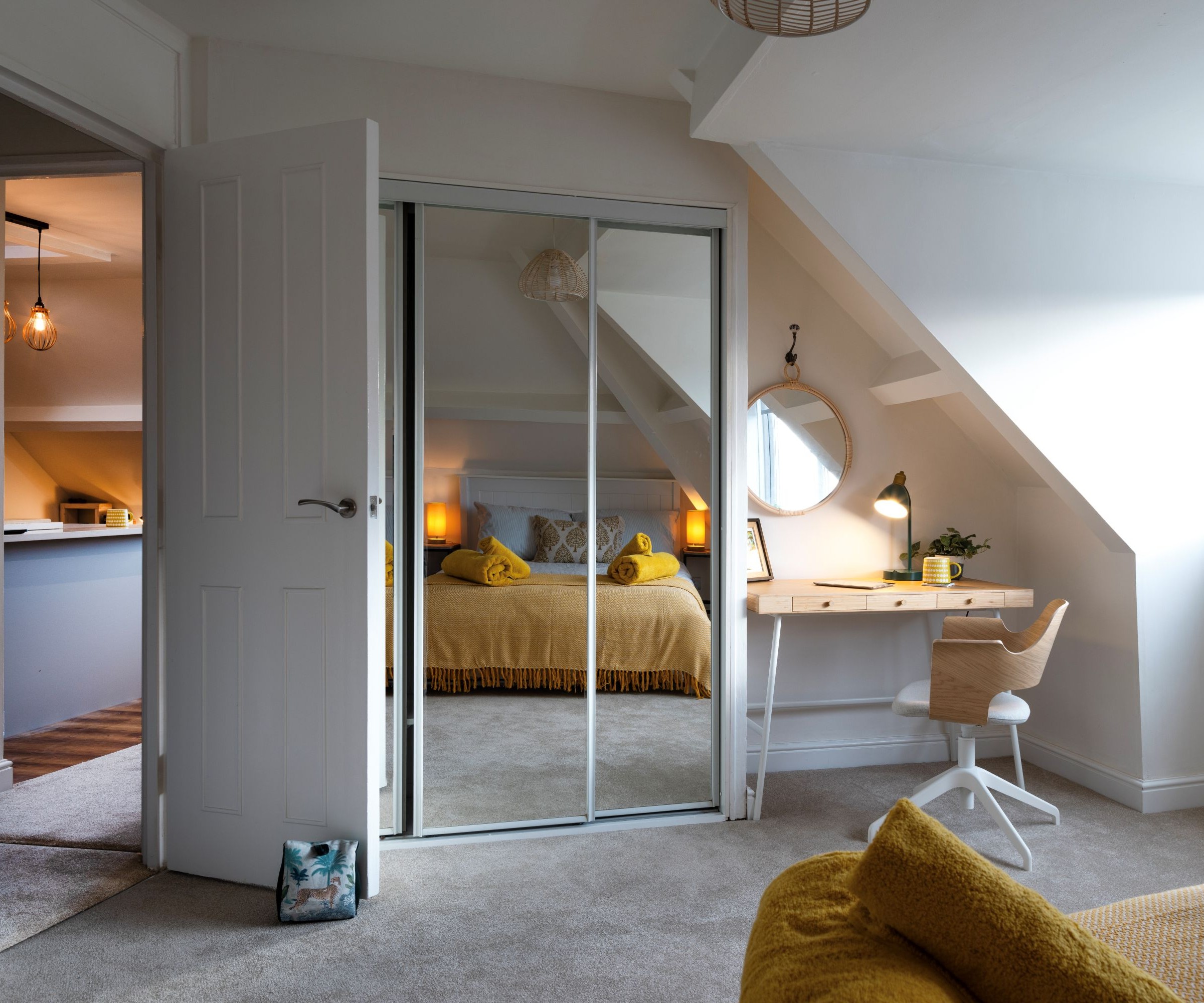 A loft conversion with a mirrored wardrobe and an open wooden door through to a hallway
