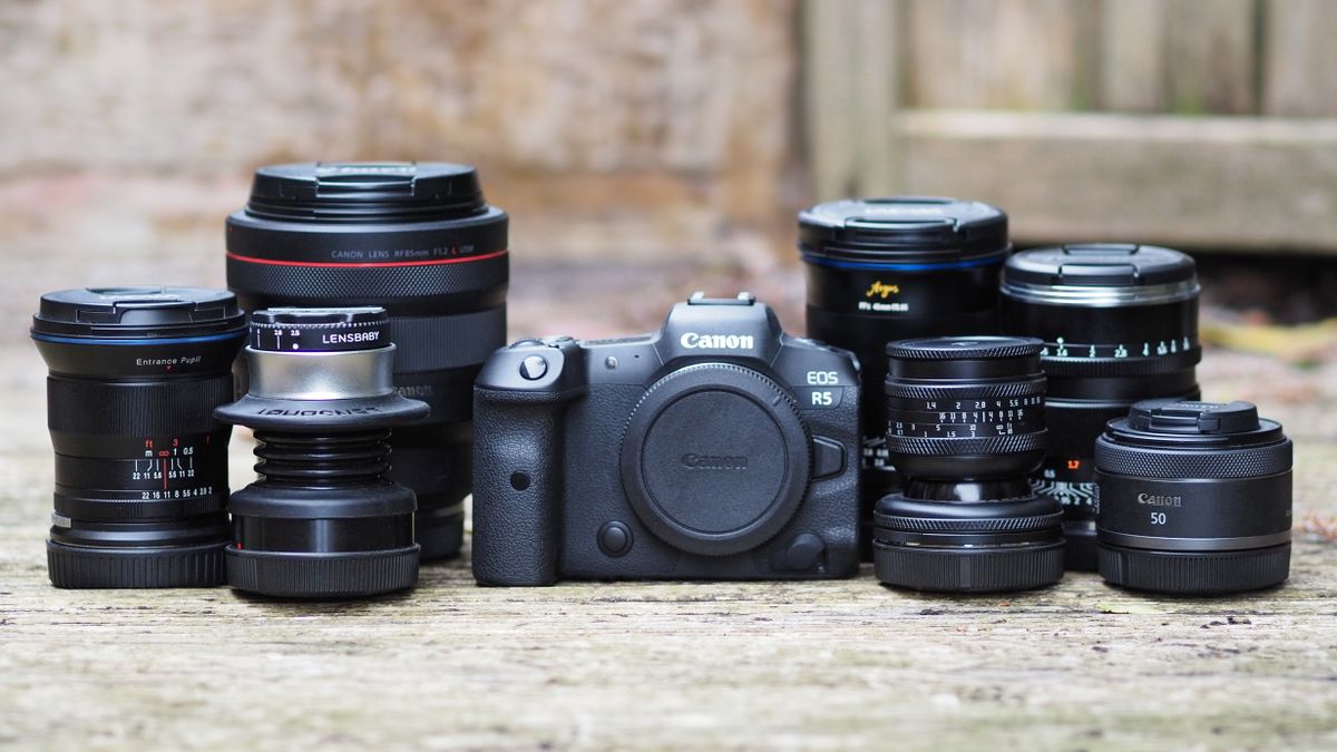 A Canon EOS R5, sitting on a wooden outdoor surface, with a selection of Canon, Laowa, Lensbaby, AstrHori and Zhongyi RF lenses