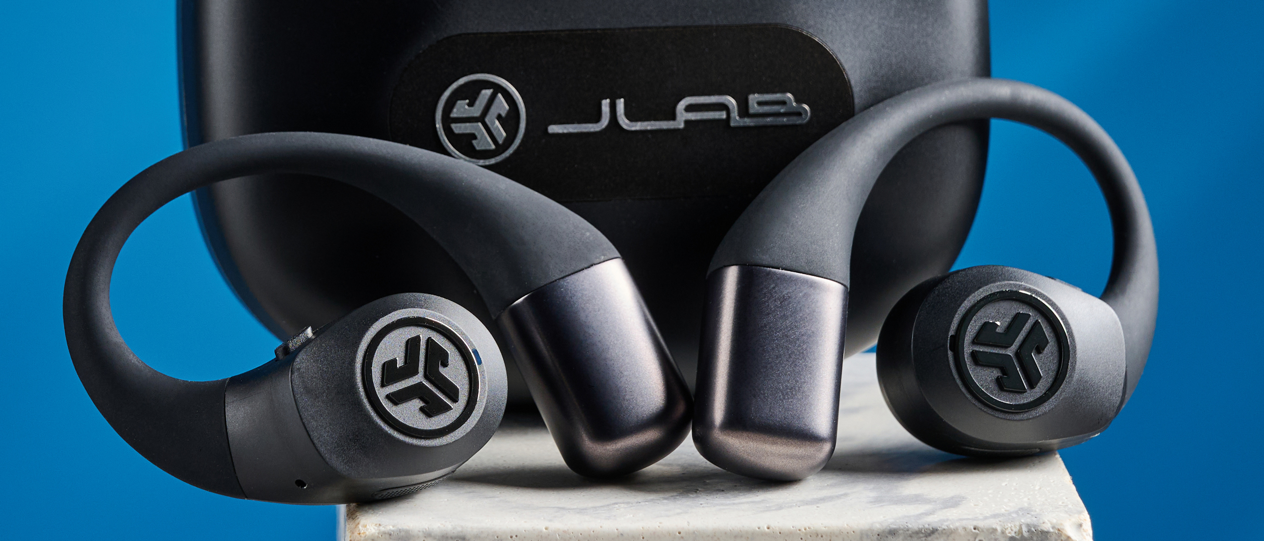 Jlab epic open sport open-earbuds in a black colorway photographed on a blue background.