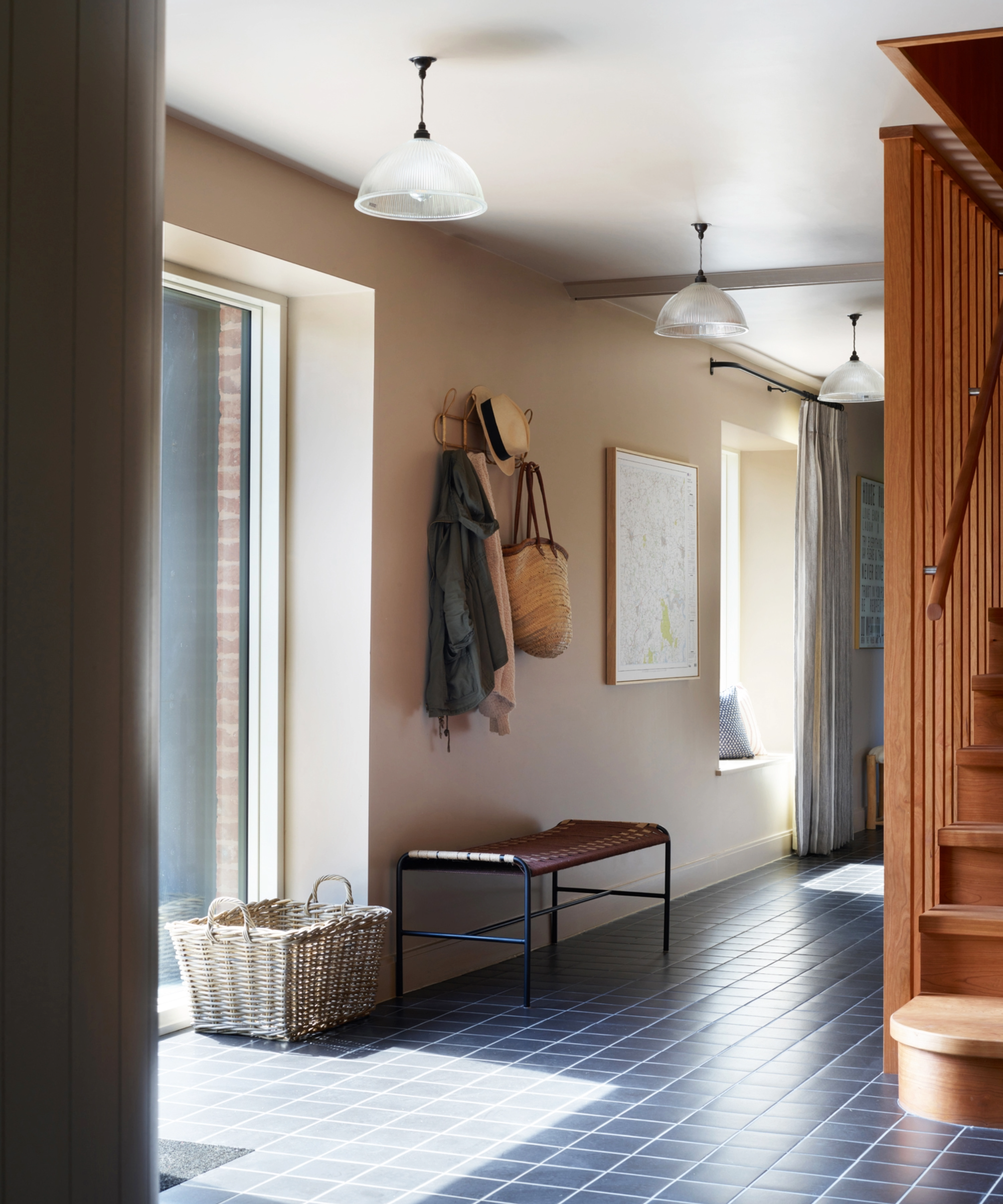 Hallway with square floor tiles, pegs for hats and coats, bench, and wooden staircase