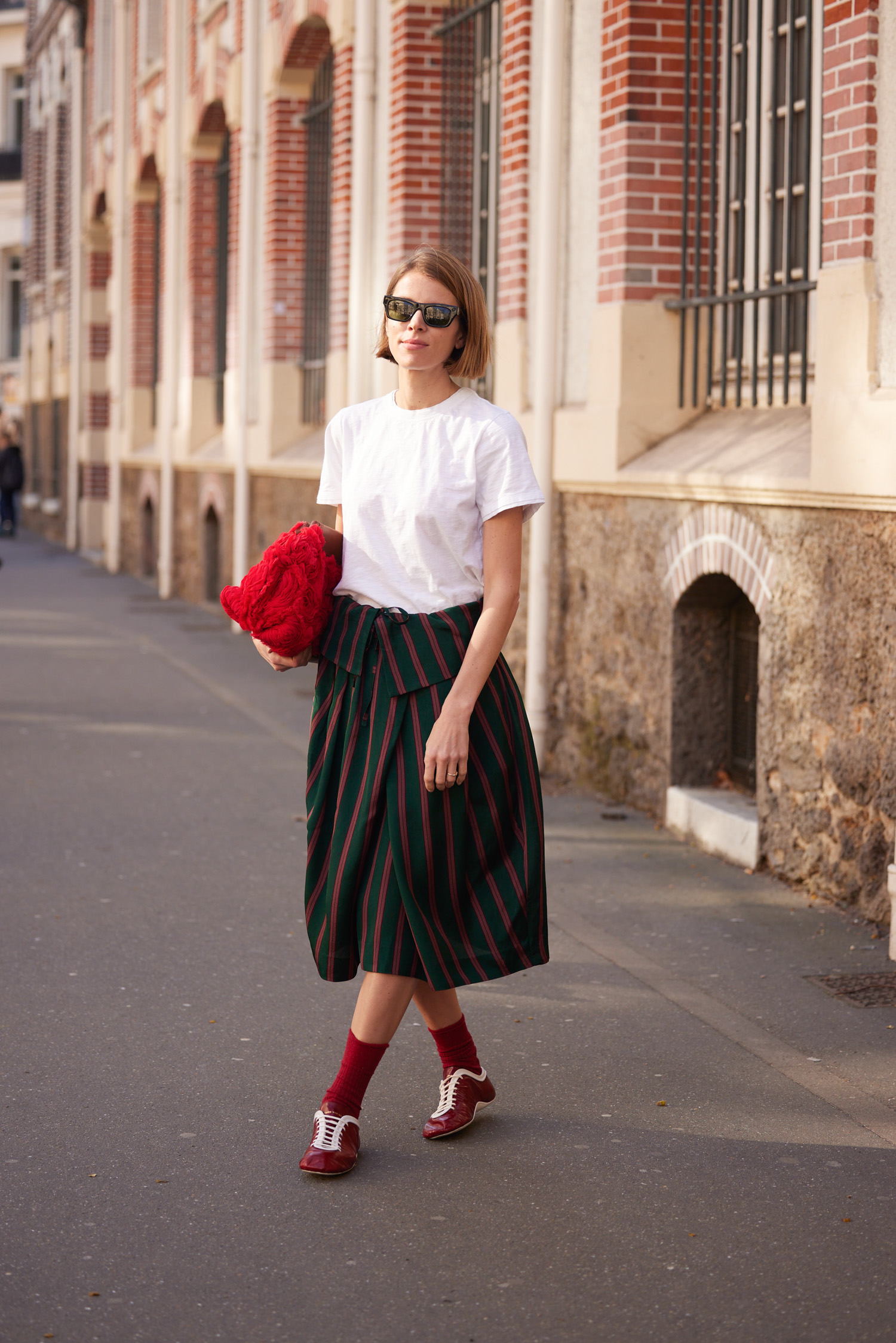 Woman in a striped skirt, white crewneck, and low profile sneakers.