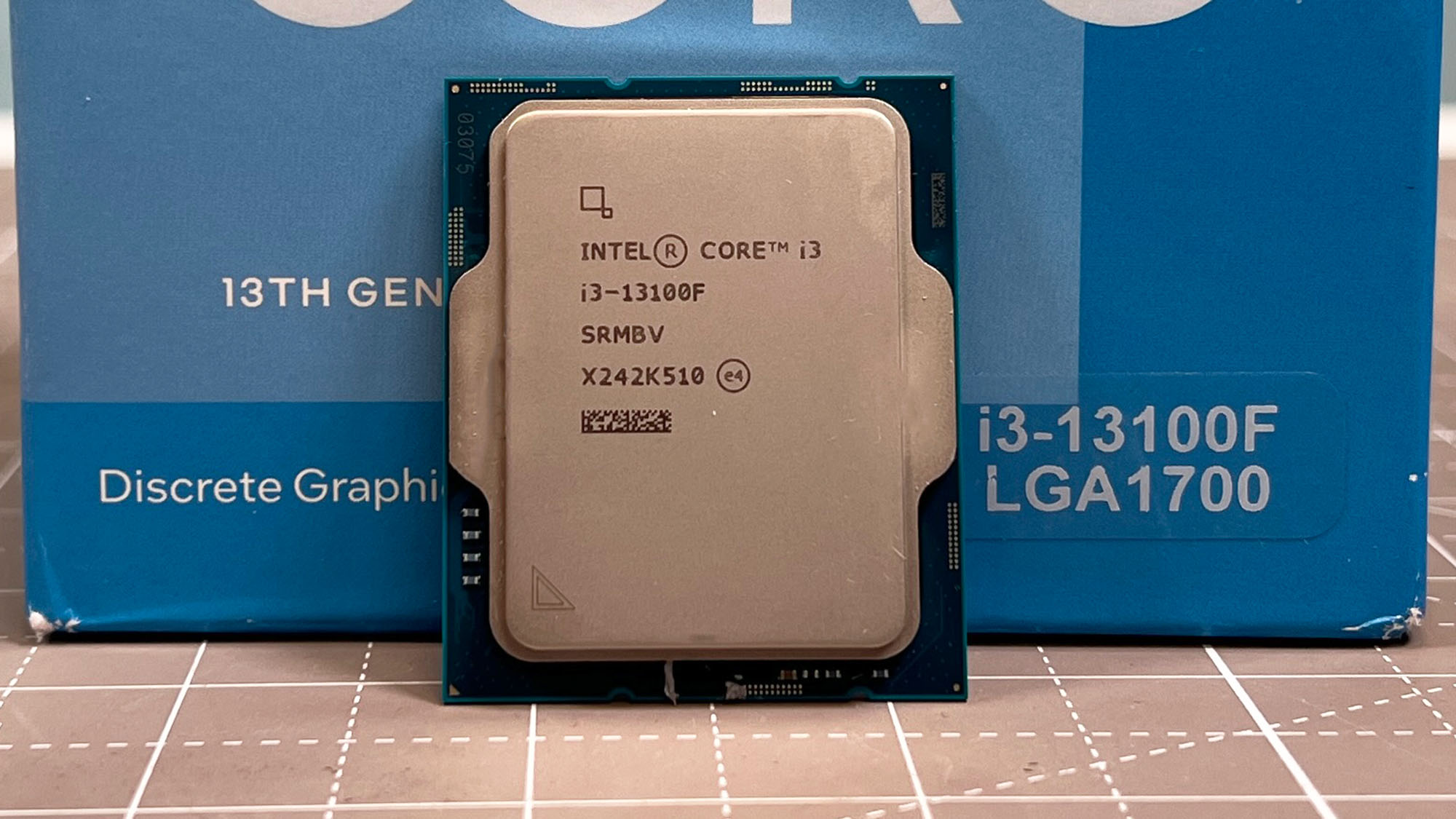 An Intel Core i3-13100F standing upright in front of its retail packaging