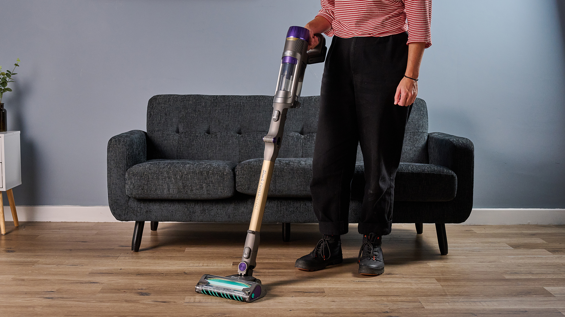 Ruth Hamilton holding Shark PowerDetect Cordless cordless stick vacuum, with a sofa and side table in the background