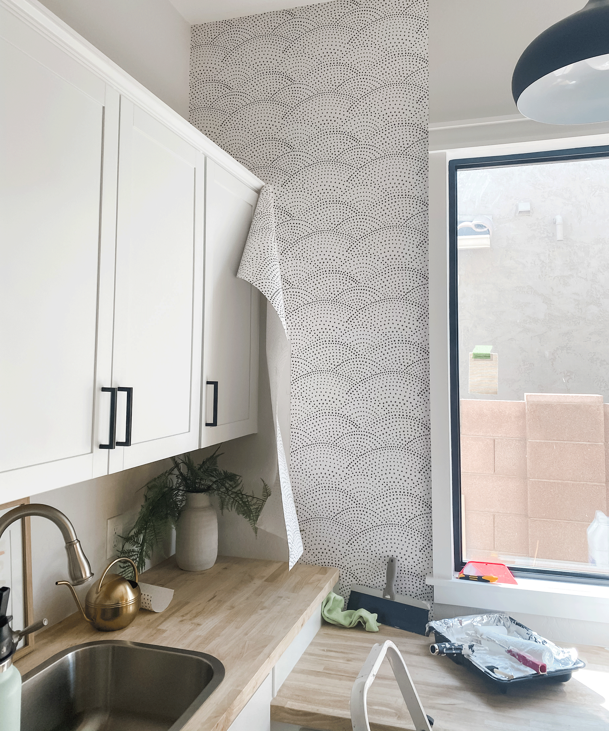 A kitchen with white cabinets with handle decor, monochrome spotted black and white wallpaper covering and modern round light fitting