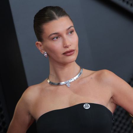 a white woman wears a strapless black gown and poses in front of a black background at a red carpet event