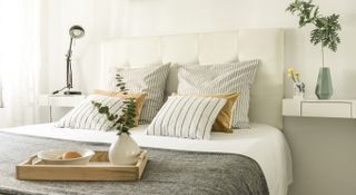 Cosy bed with white and grey bedding and pillows with a tray placed on the edge of the bed