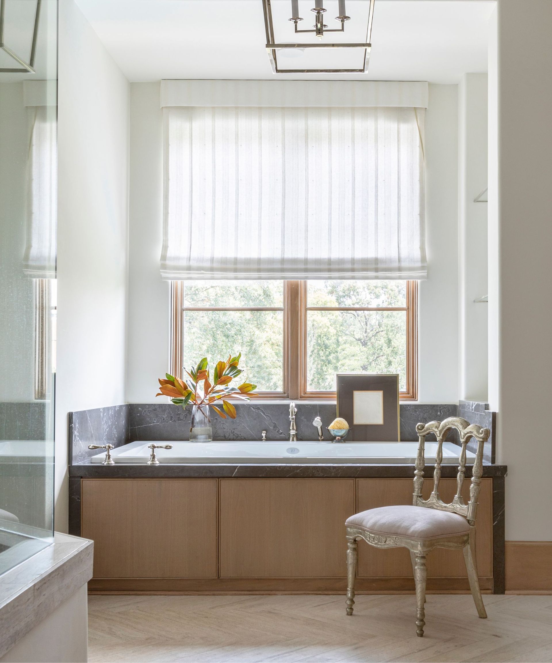 A bathroom with an alcove bathtub clad in wood panels with a dark marble backsplash and surround