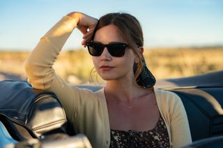 Jenna Coleman as wife Liv in the Wilderness cast wearing a yellow cardigan and sitting in a car. 