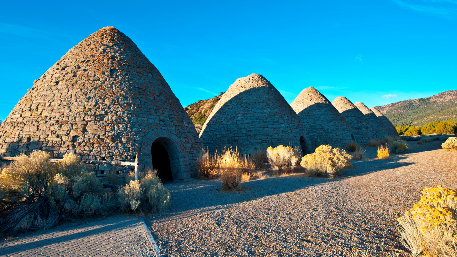 A row of stone huts with roofs tapering to a point against a blue sky.